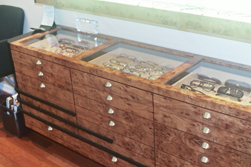 Bespoke burl-veneer optical display cabinet with glass-topped cases and brass pulls, custom made by Van Aken Design